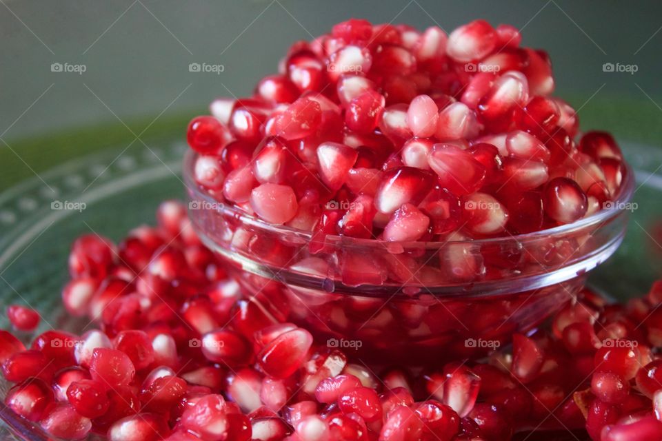 Fruits! - Closeup of fresh pomegranate seeds overflowing a small glass bowl against a green background