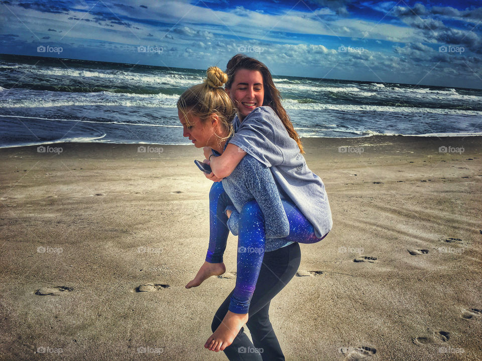 Woman carrying her friend piggyback ride at beach