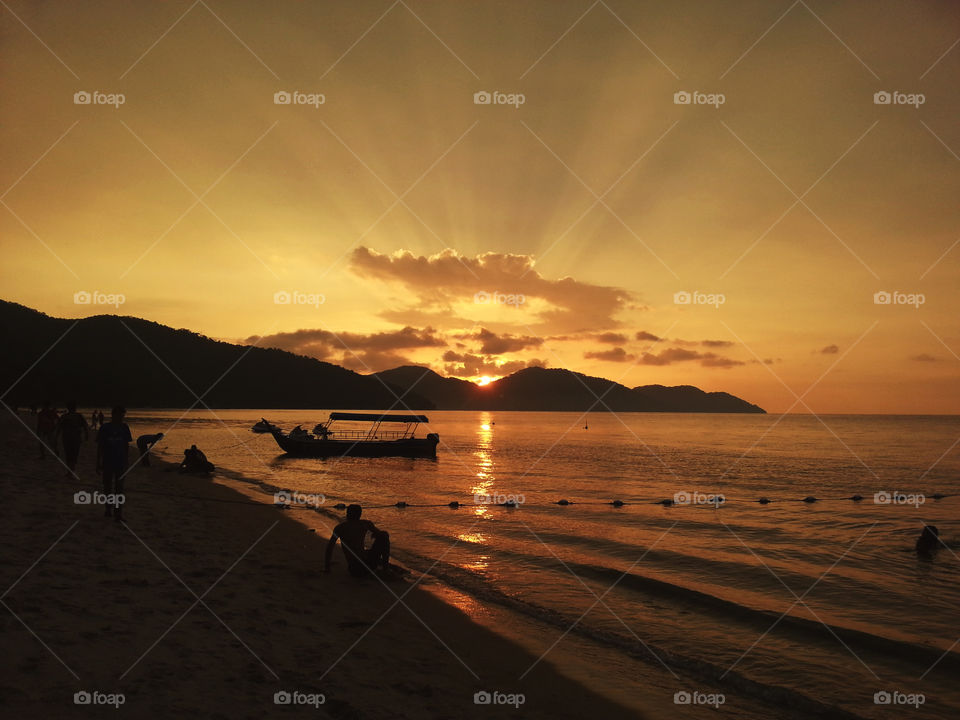 Orange sunset view with silhouette of hills, boat and people enjoying the beach and beautiful scenery