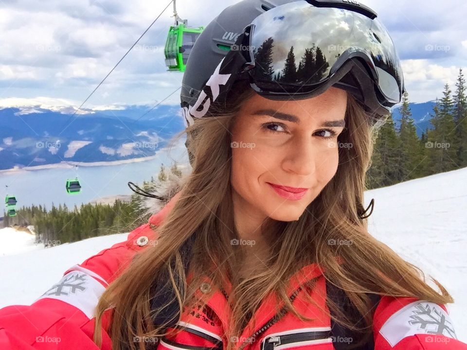 Portrait of woman skier wearing Uvex ski glasses and Uvex helmet with ski lifts in the background 