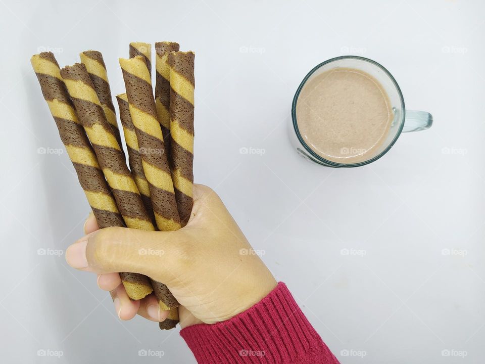 Holding some wafer roll sticks and a glass of chocolate milk on white background. Top view