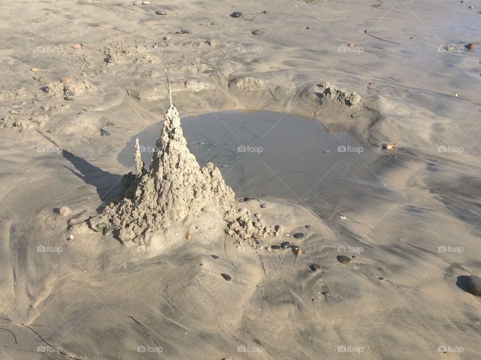 Sandcastle standing before its own tiny lake. 