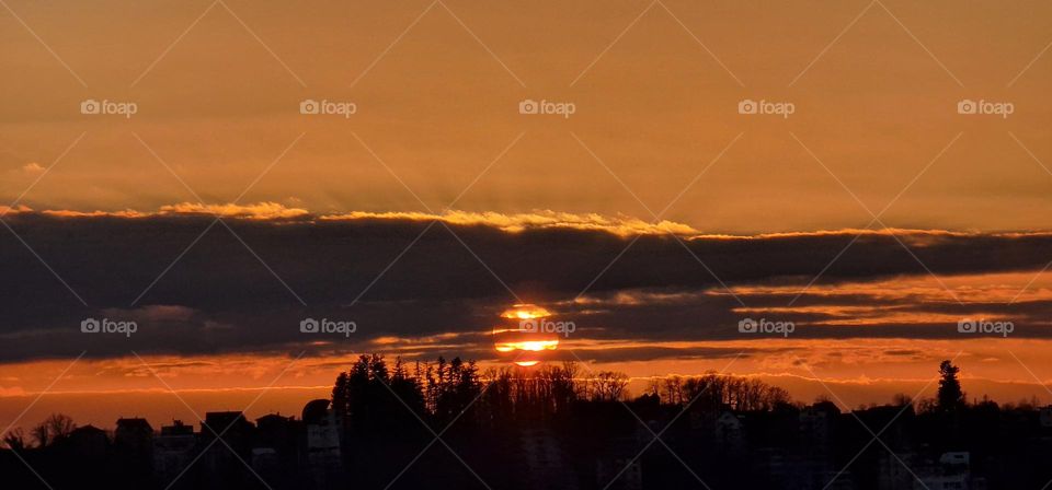 Sunset while cloud and sun cross their paths on the horizon