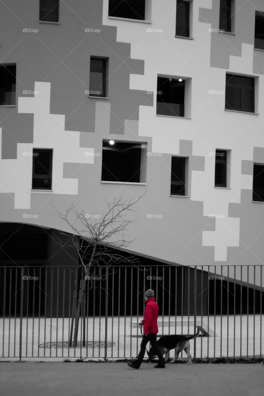 Young woman in red jacket walks her dog in front of the modern building.