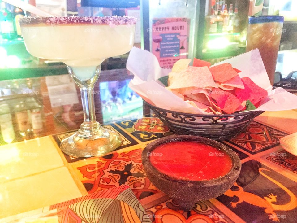 Margarita, tortilla chips and a bowl of salsa on a bar at a Mexican restaurant
