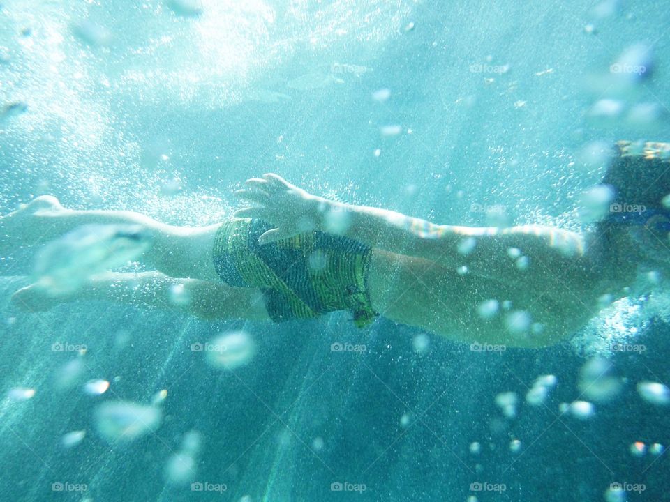 Side view of a shirtless boy swimming underwater
