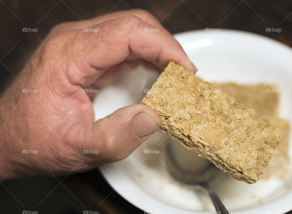 A weetbix biscuit being placed in a cereal bowl for breakfast.