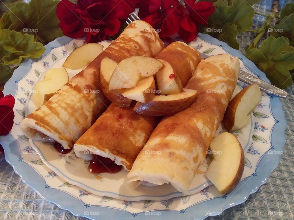 rolled pancakes with Apple on blue and white plates red flowers in background