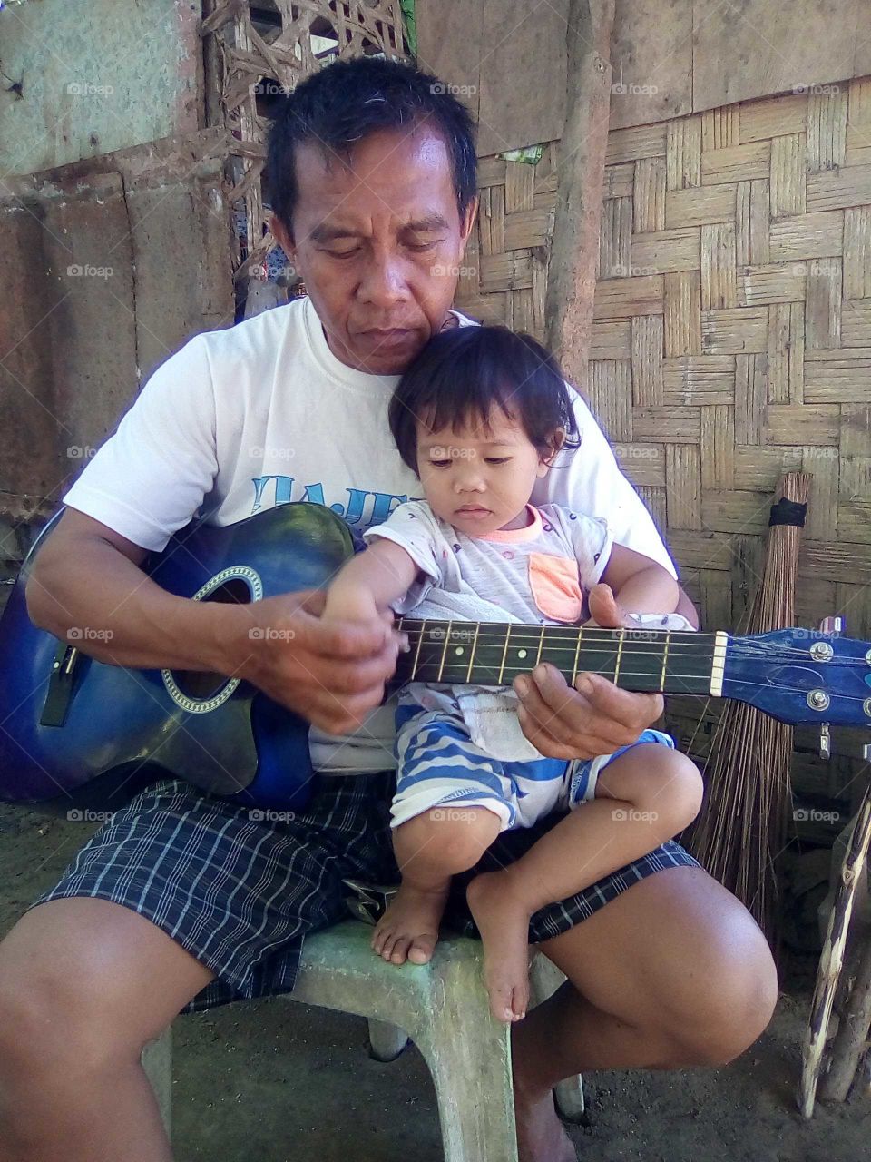 My father is trying to show my baby sister how to strum the guitar. It is good to see that they are interacting with one another.