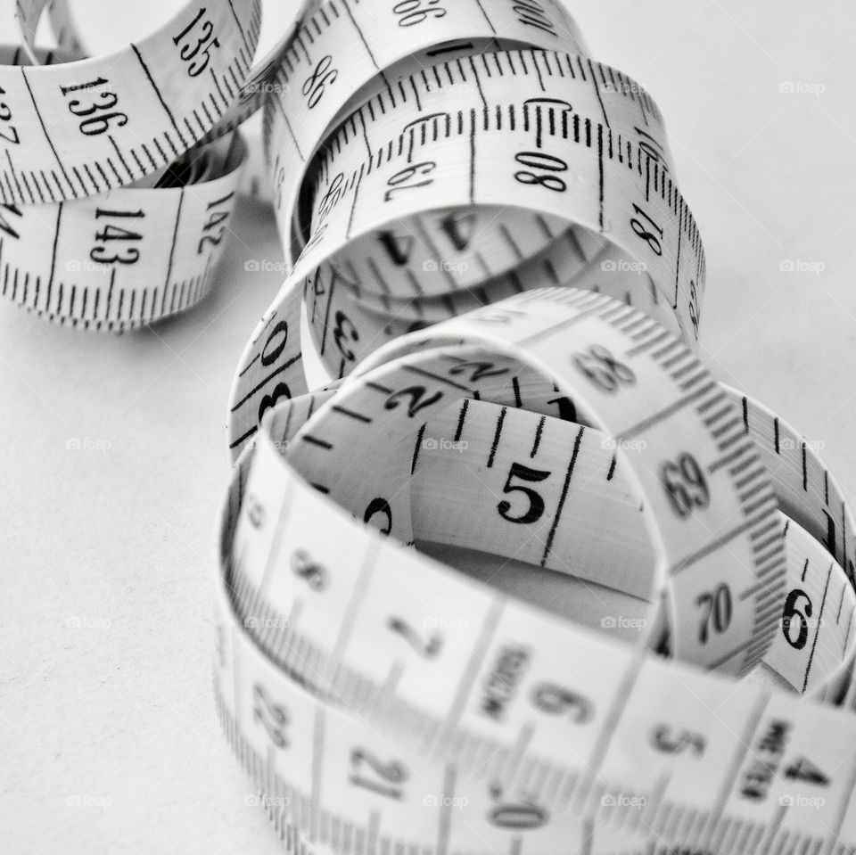 Tape measure, coiled, in close up and black and white showing numbers. Metric and imperial. Inches and centimetres 