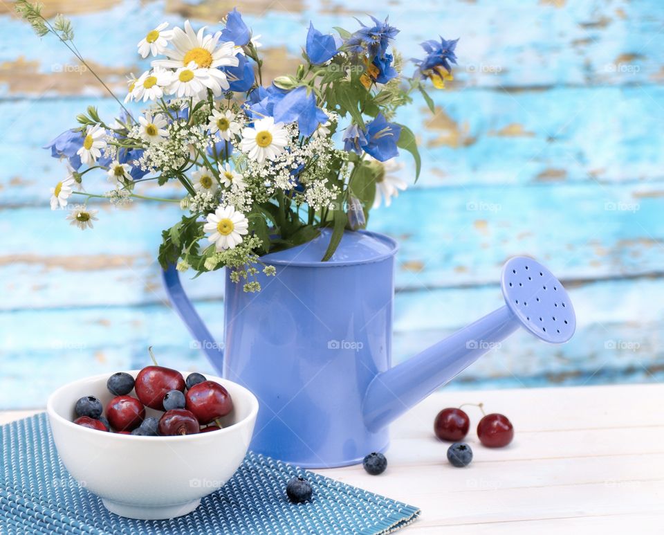 summer still life watering can with wildflowers and a plate with cherries and blackberries 