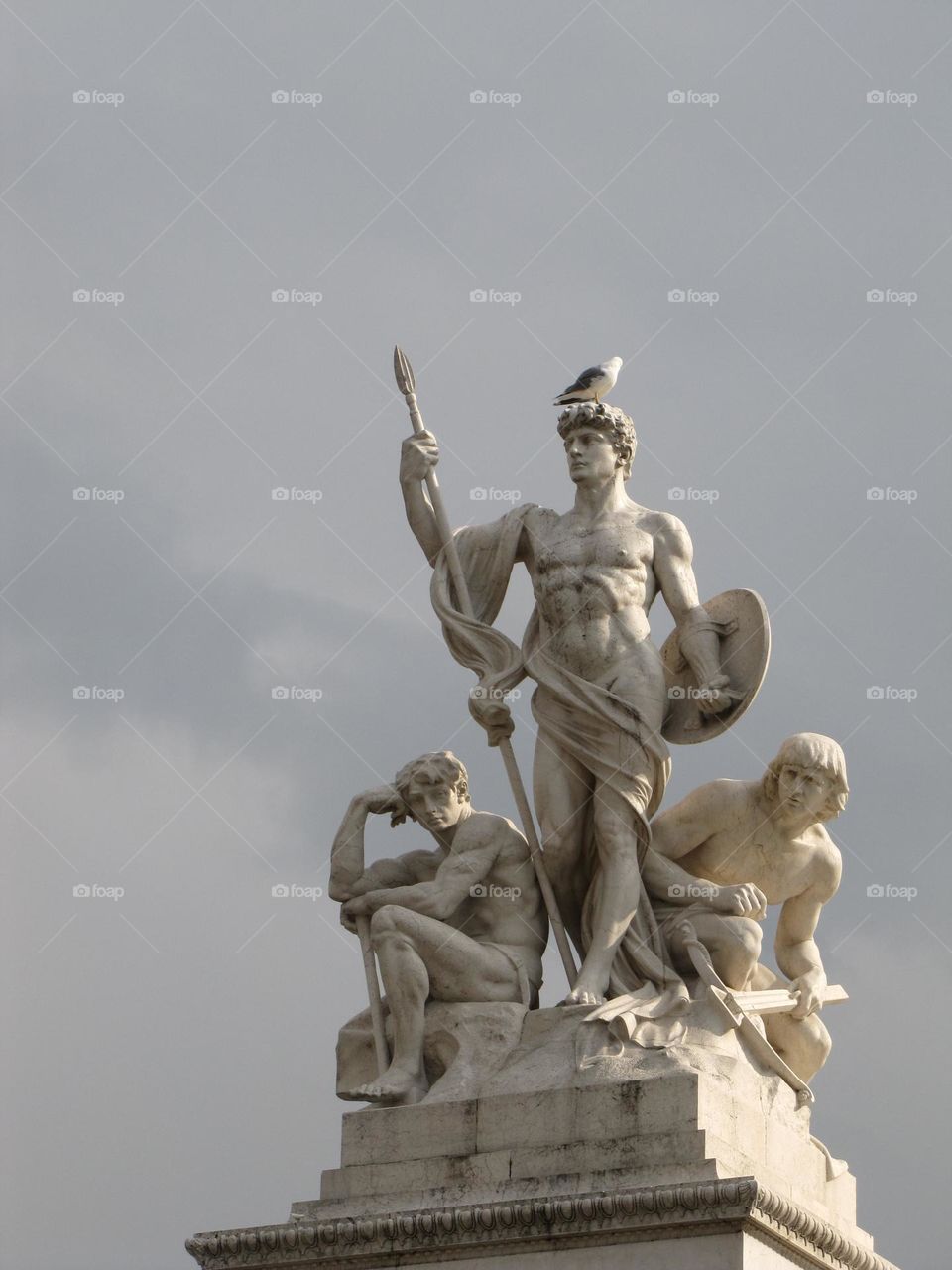 Una estatua de tres hombres con distintas poses y elementos, una paloma real posa sobre la cabeza del hombre del medio.