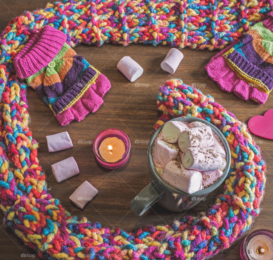 Multicoloured, knitted scarf and gloves with hot chocolate and candles on a wooden background 