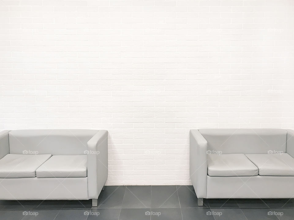 Minimal elements of interior design with a couple of grey sofas on pastel brick wall background on geometric pavement 