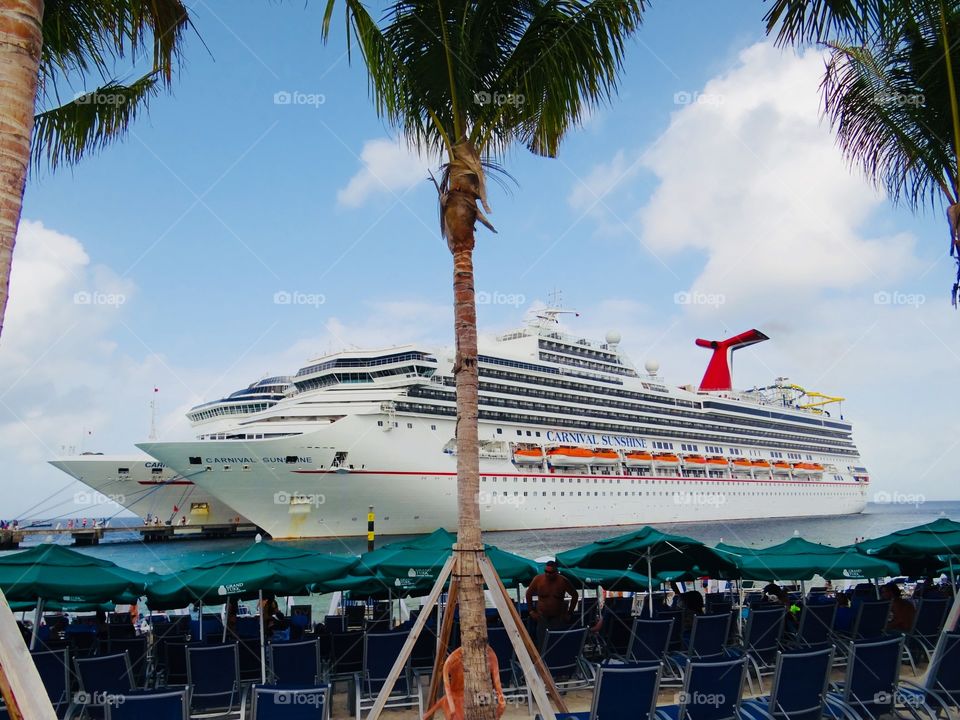 Cruise ships docked on port. Beach chairs and umbrellas inviting the travelers to seat and relax. Palm trees swinging with the ocean breeze.