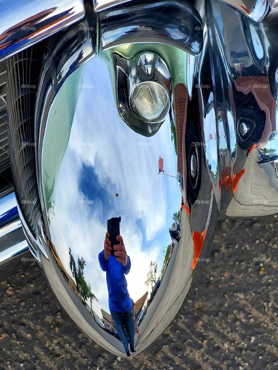 My reflection is shown in a highly polished chrome bumper piece of a classic 1950's Cadillac