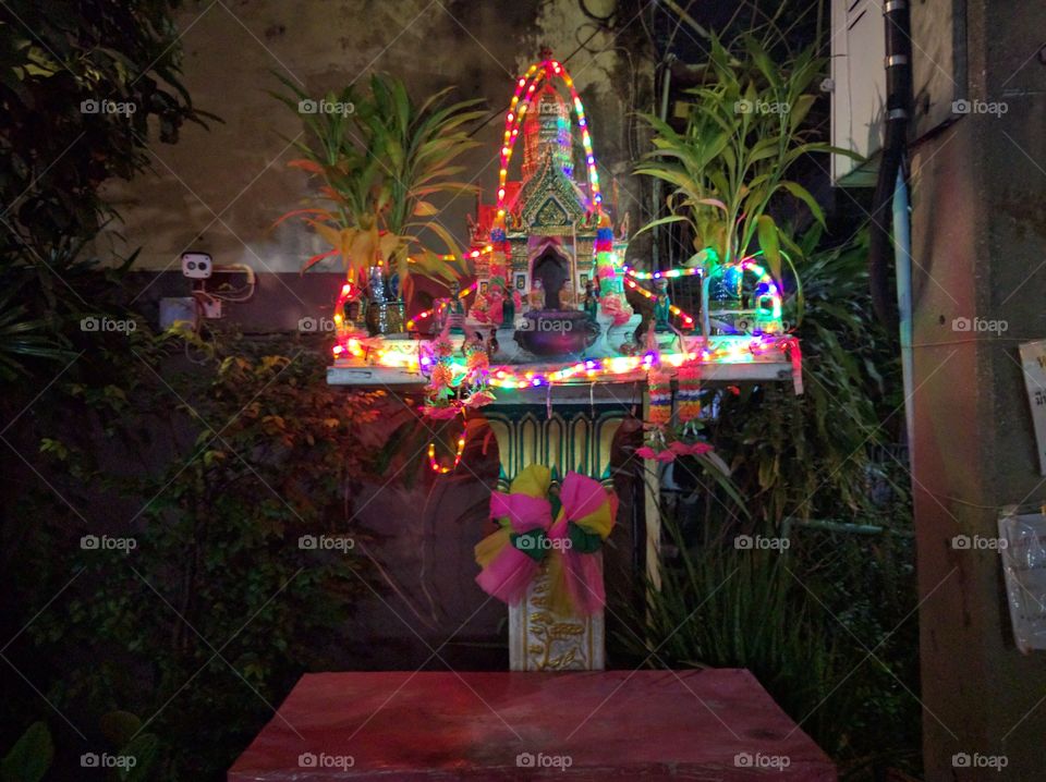 A small buddist shrine in a street of bangkok by night