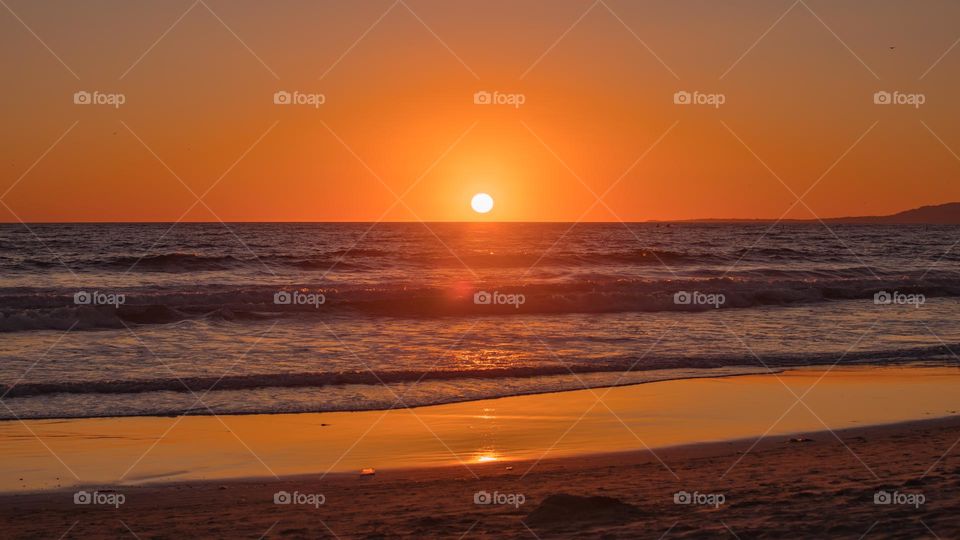 Sunset twilight at Santa Monica Beach in Los Angeles California. Dim natural light reflect onto the calm water with small waves. Facing west over the Pacific Ocean.