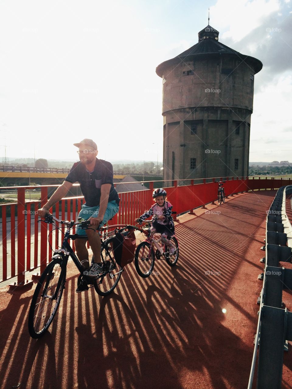 Father and daughter cycling on bridge in city