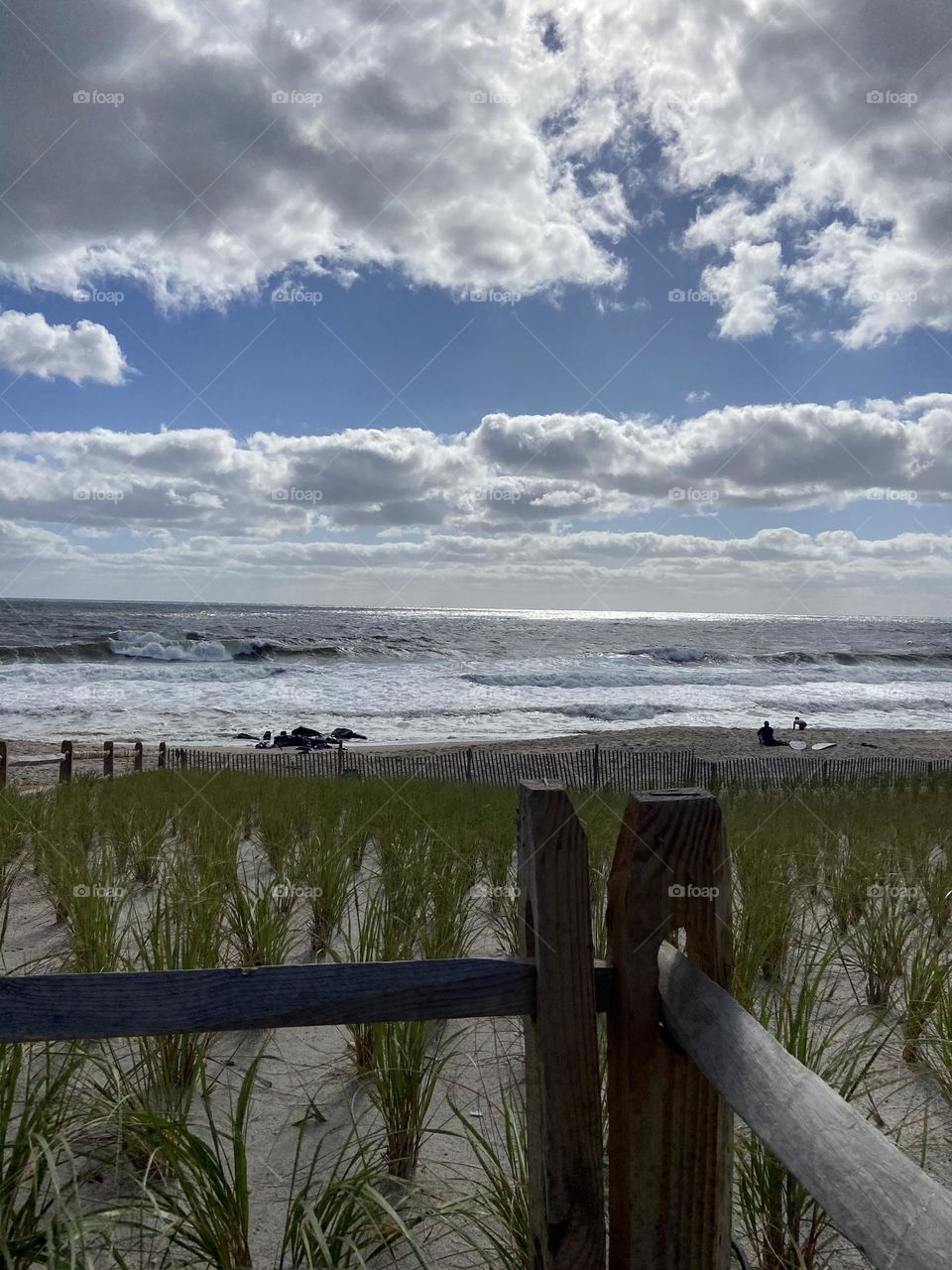 When I look at this photo, my eyes are drawn to the clouds that frame the blue sky. The corner of the fence is aligned with the vertical break in the clouds on the right, and the whitecaps in the ocean resemble another line of clouds on the sand.