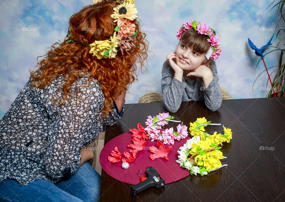 Mom and daughter make beautiful wreaths on the head of artificial flowers.