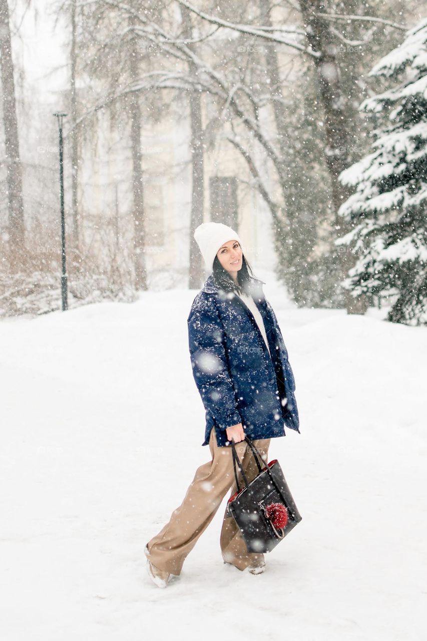 A beautiful young girl walks in a winter park during a snowfall.