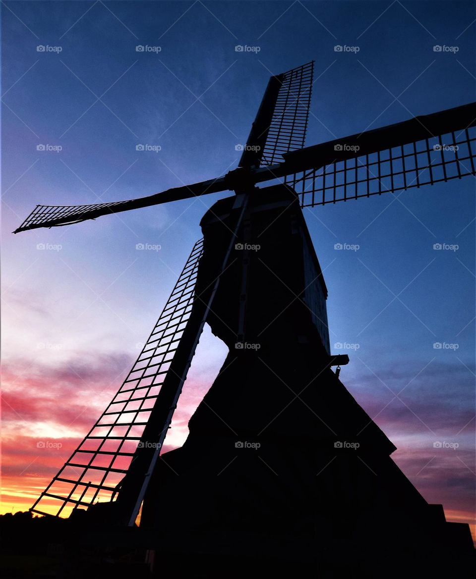 black silhouette from a Dutch windmill at dawn with large windmill wings and colorful skies at the background