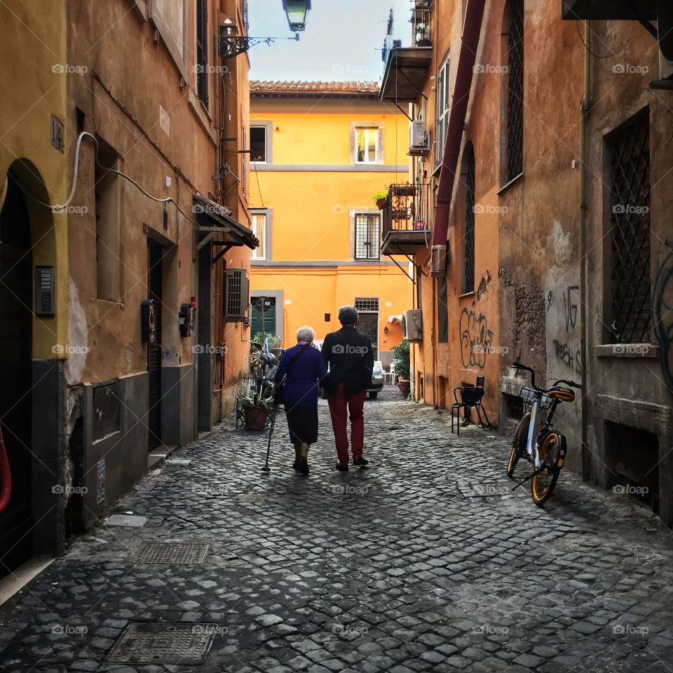 Two people walking on a side street in the Trastevere neighborhood of Rome