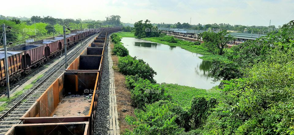 Railyard view with freight cars,wagon,containers at sunset surrounded with green trees and small pond,Captured at the daylight.