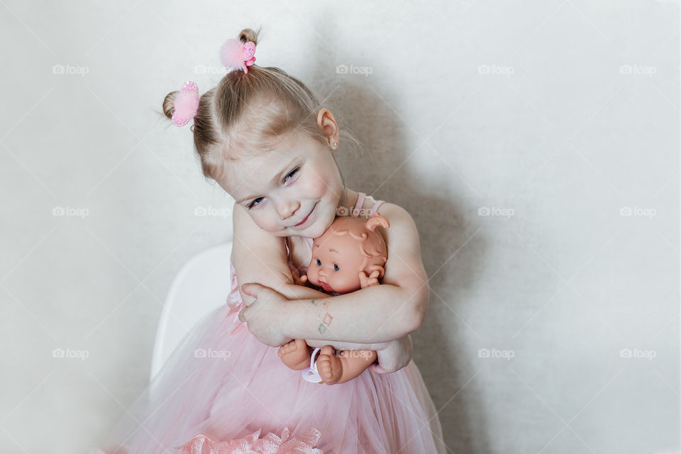 girl in a pink dress smiles and hugs her doll