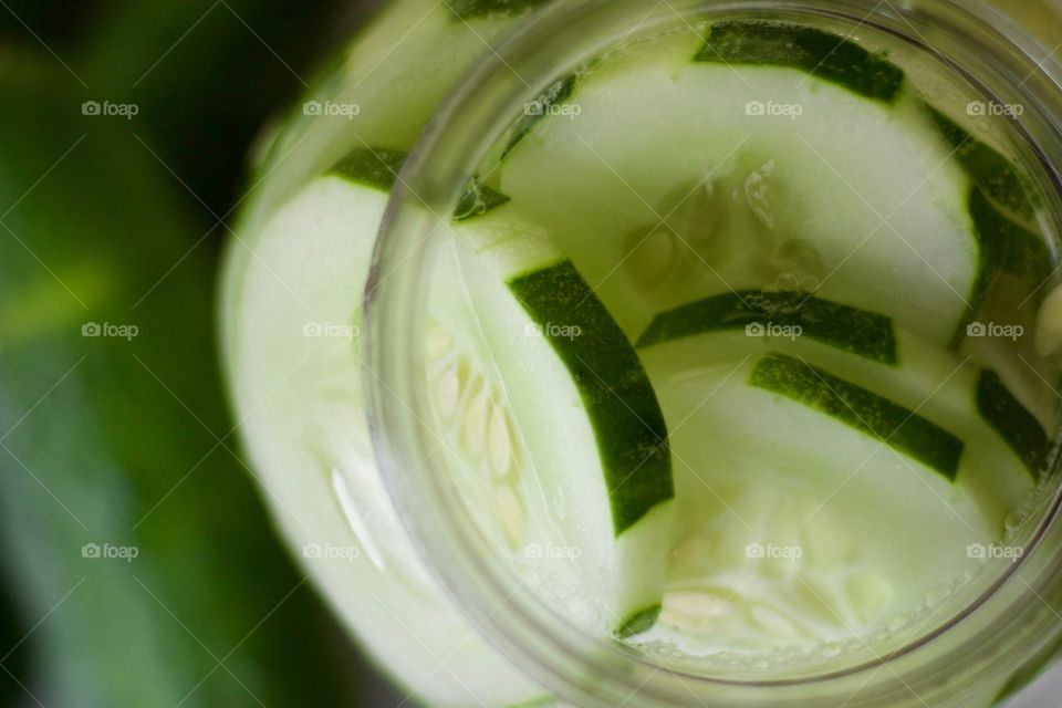 Overhead view of cucumber-infused water in a half-gallon mason jar, with cucumbers on a white dish towel