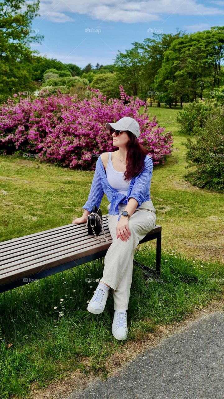 Young woman in a cap and blue shirt sitting on a park bench