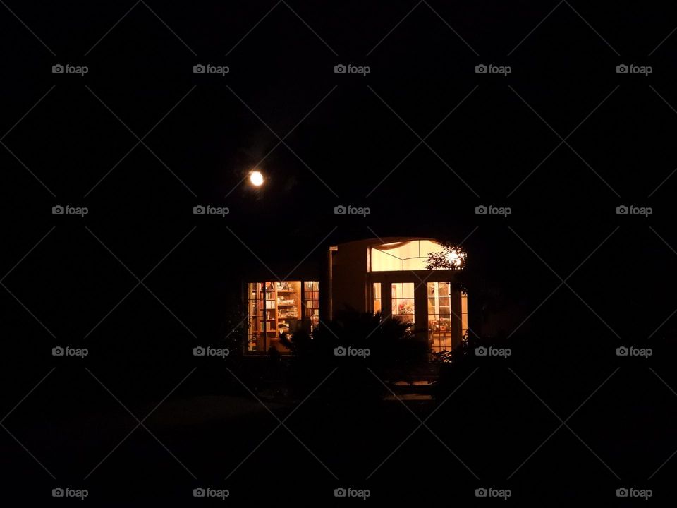 Warm light through windows with rising moon in background 