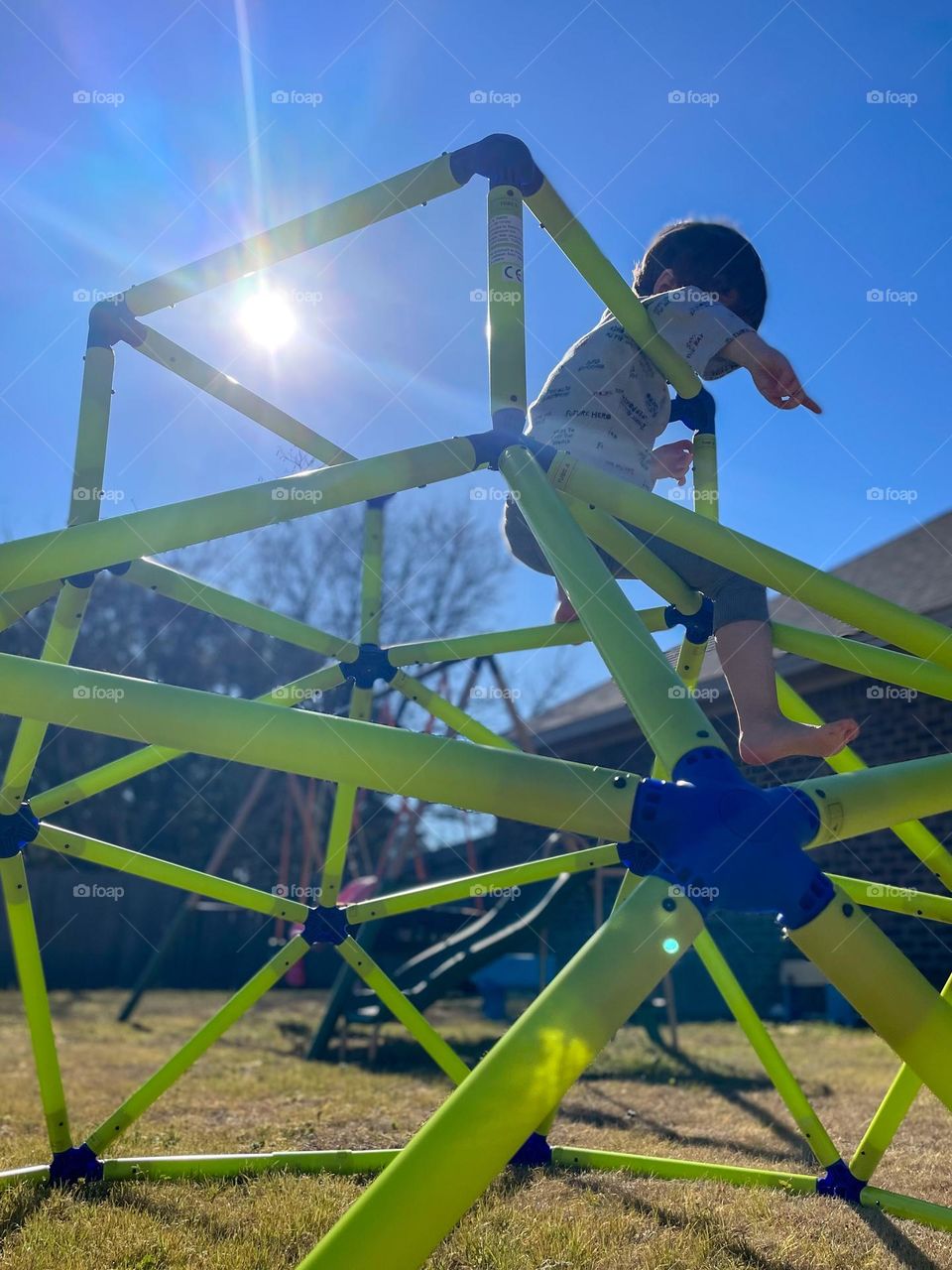 Looking up to a child playing on a jungle gym, the bright sun outlining his tiny form