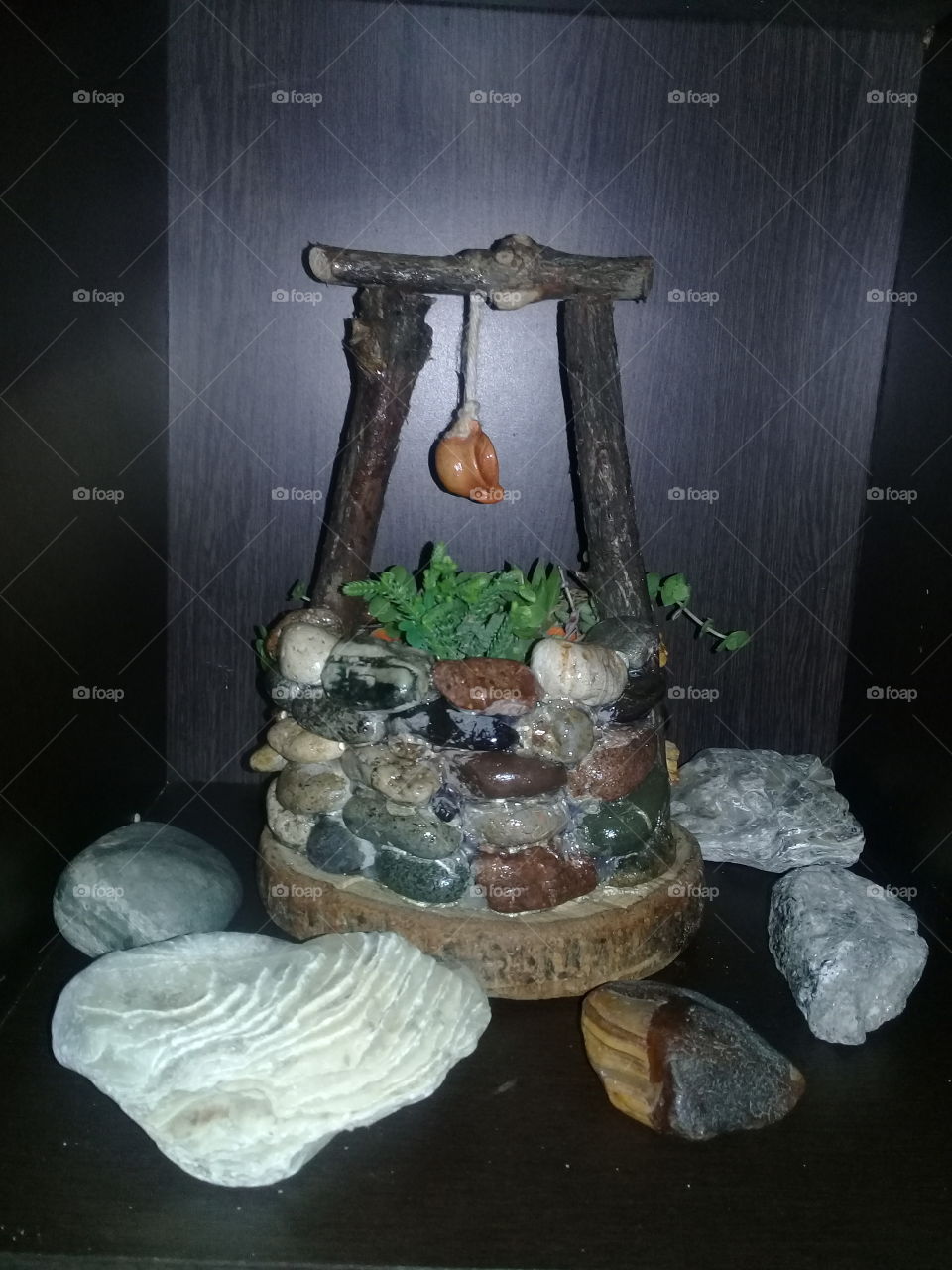 pequeño aljibe realizado en piedra u troncos, rodeado de piedras y caracoles, con una pequeña maceta con suculentas de varias clases.