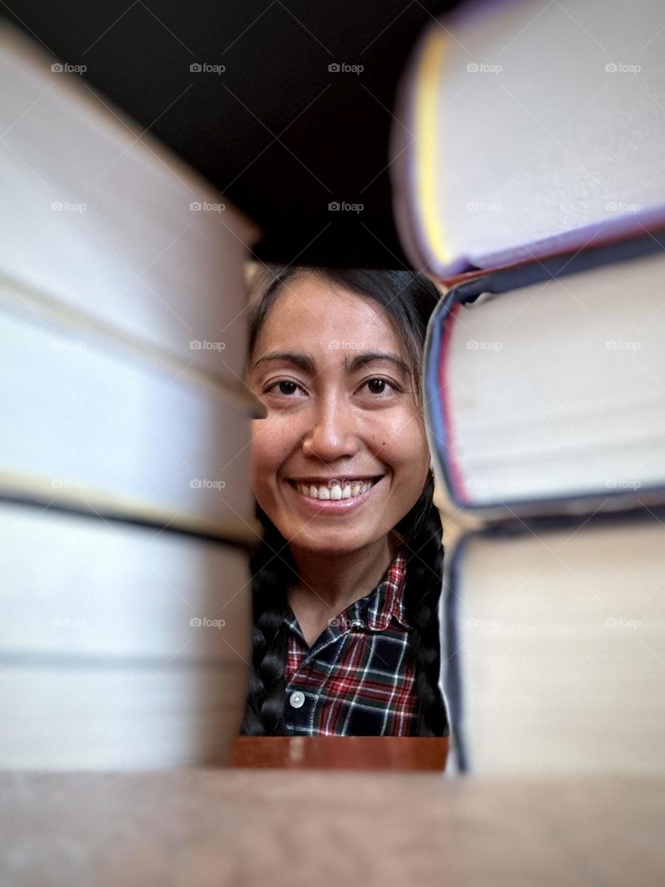 Smiling happy woman peeping with braided hair and stripes casual clothing with books background. 