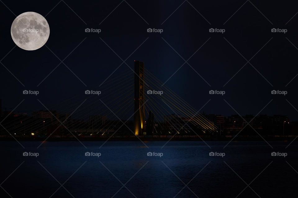 Evening photo with the moon in the sky over the bridge that transits the city.