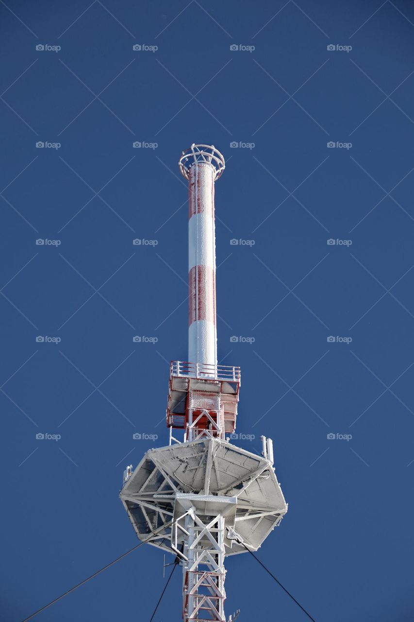 Icy and snow-covered red and white transmission tower under a blue clear sky 