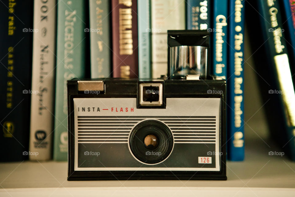 A vintage, black, insta-flash camera from my personal collection of antique cameras and books as a backdrop. 