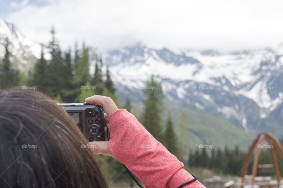 Woman wearing long sleeved red shirt holding camera photographing snow capped mountains in western Canada 