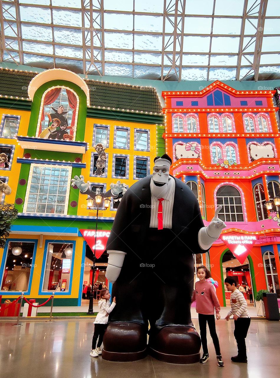 Amusement Castle. Children near their favorite character "A huge monster, Dracula's friend." In the background, multicolored facades of buildings