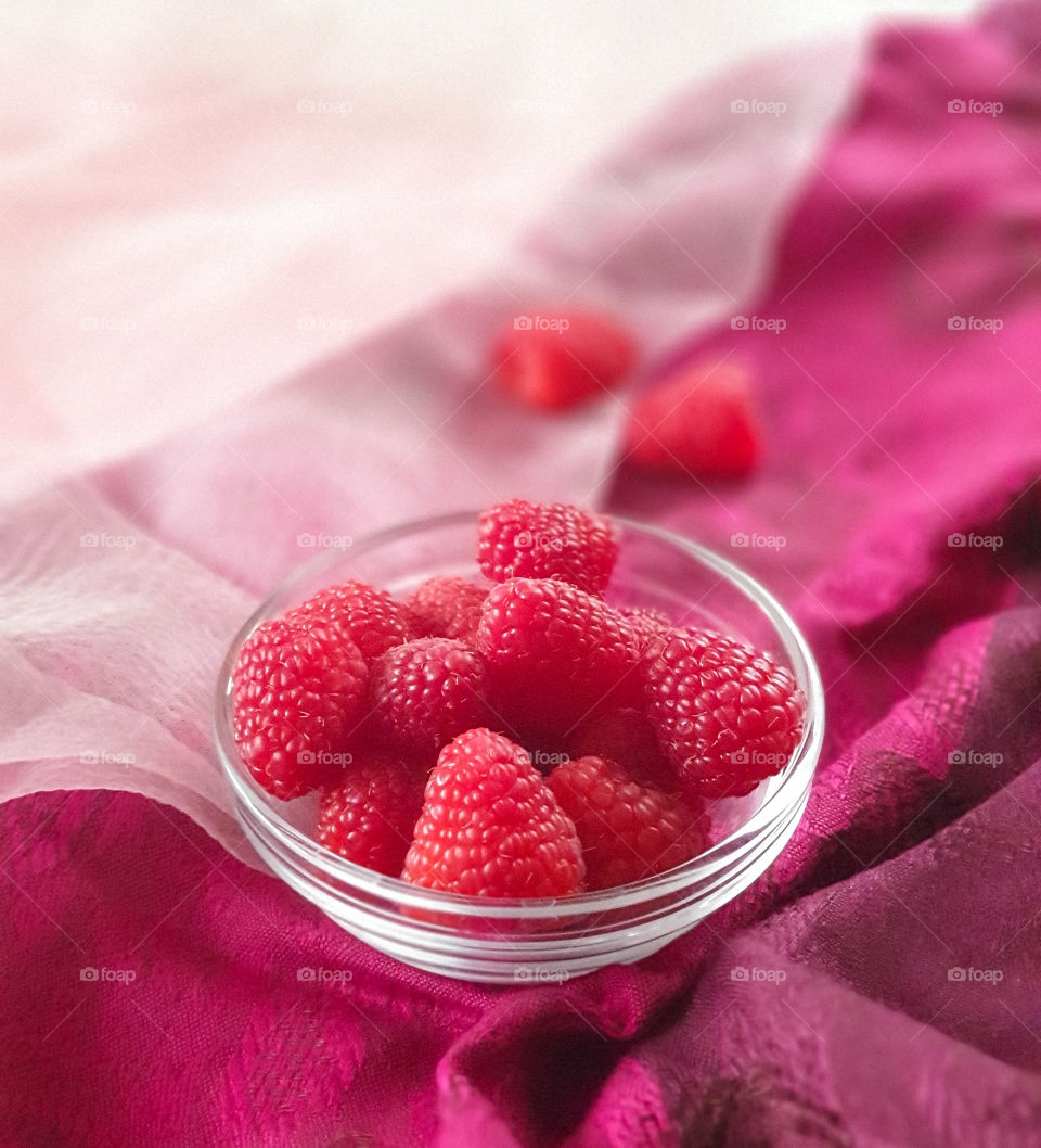Glass bowl with fresh raspberries on pink textile.  Healthy, tasty snack.  Simple natural food concept.  Food photo
