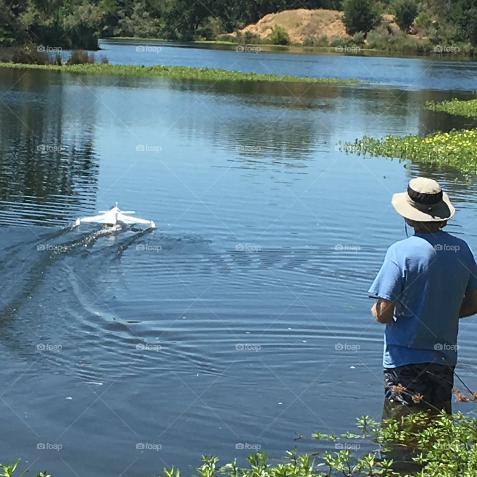 Man in water lake marsh operating a remote control drone watercraft boat