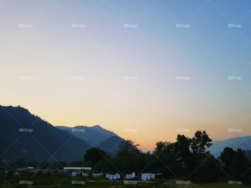 The blue silhouette of mountains during the sunset in Nepal. White sheets hanging in the foreground.