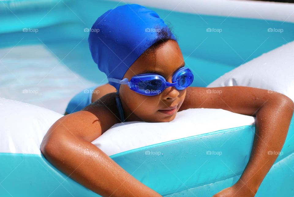 Girl of mixed race enjoying the refreshment of water in a swimming pool on a hot summer day, together with her little sister (family, fun, summer, water, blue, swimming suit, splash, hot, enjoy, play, outdoors)