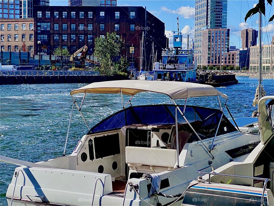A large industrial barge is floating by behind the motorboats that are moored here at „Newtown Creek“ by the „Pulaski Bridge“ in LIC, Queens on a bright sunshiny afternoon in October 2023. Hypnotic Productions