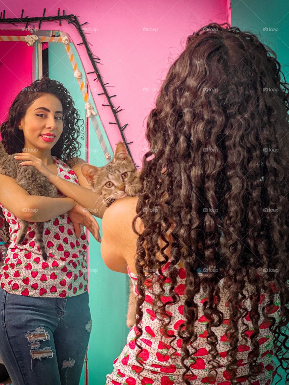 Curly haired girl hugging a kitten in pinky room