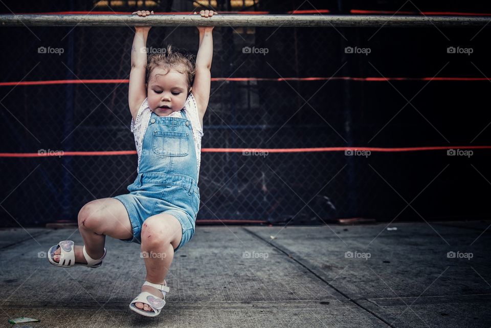 Young girl in dungarees hanging from pole