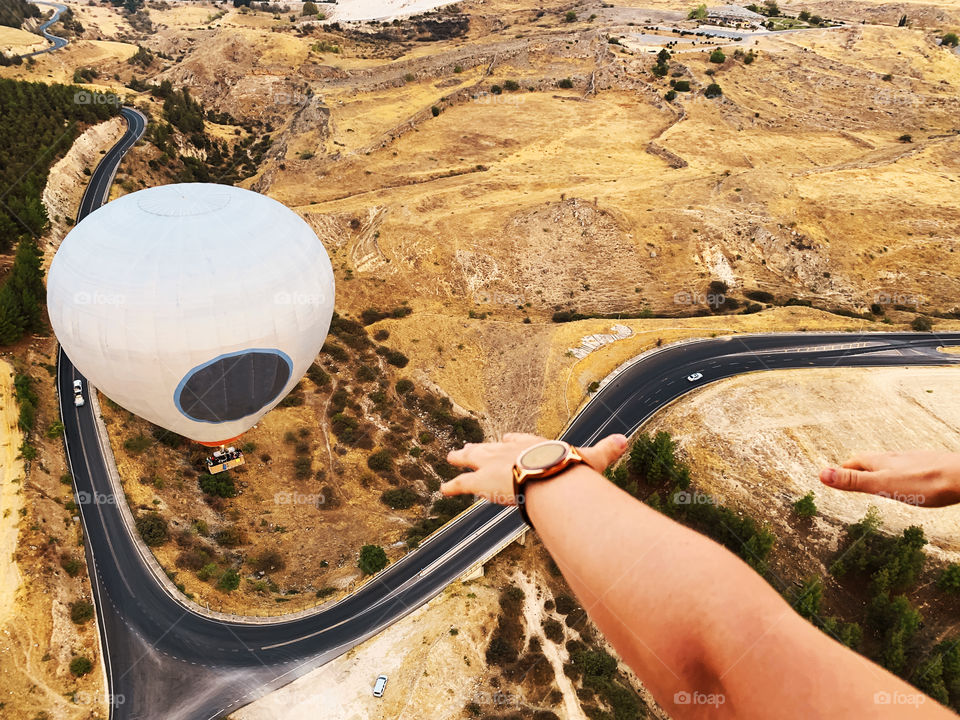 Hands trying to touch hot air balloon flying over the beautiful landscape with open road and moving car on it 