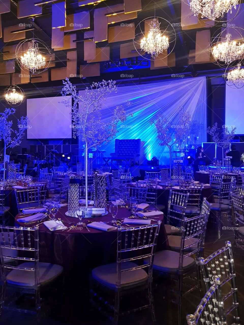Organized chairs and tables under those sightseeing and shimmering chandeliers inside a modern hotel, where a special celebration will be held.
